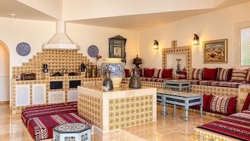 Amplia sala de estar con una mesa de centro, sofás con cojines estampados, un muro decorativo con azulejos y un jarrón grande.