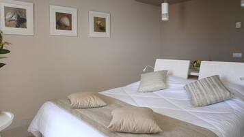 Una cama bien hecha con una colcha color beige y almohadas, una mesita de noche con un florero y tres cuadros en la pared.