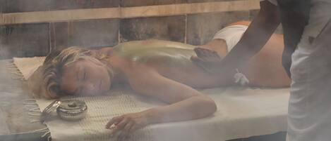 A person lying on a massage table in a steam room.