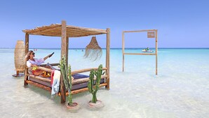 A wooden bed with a thatched roof, a cactus, and a beach view.
