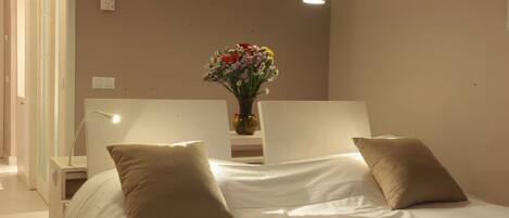Une chambre à coucher bien rangée, avec un lit, deux tables de chevet, un vase de fleurs et deux lampes suspendues.