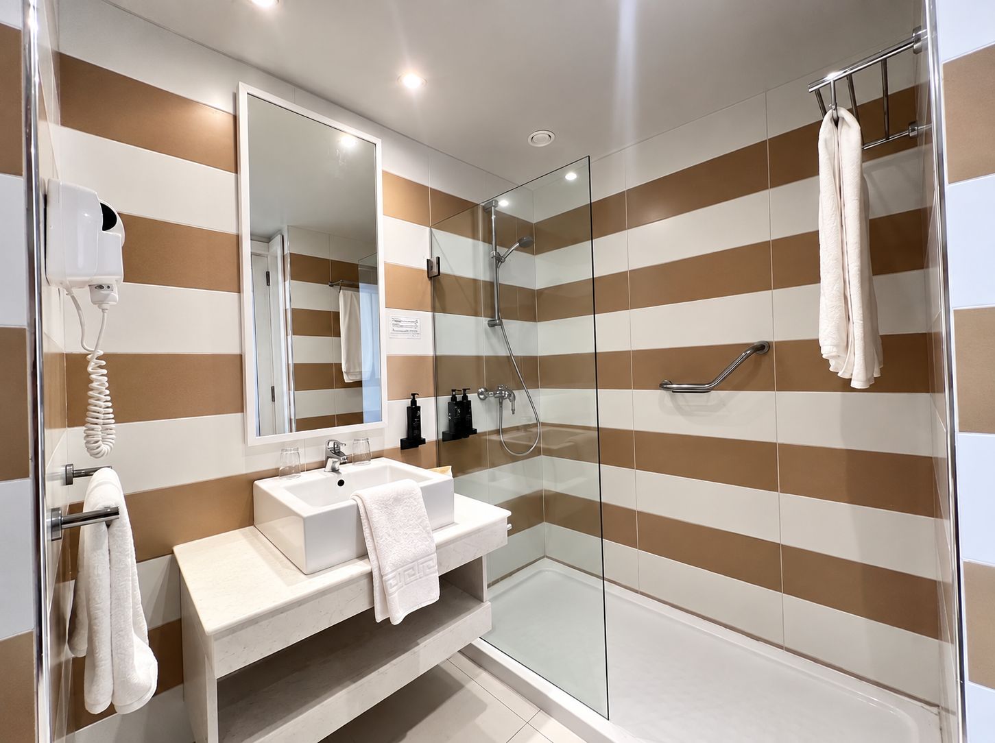 Une salle de bain moderne avec une douche à parois de verre, un lavabo blanc et un grand miroir.