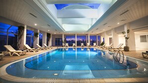 An indoor swimming pool with lounge chairs and large windows.