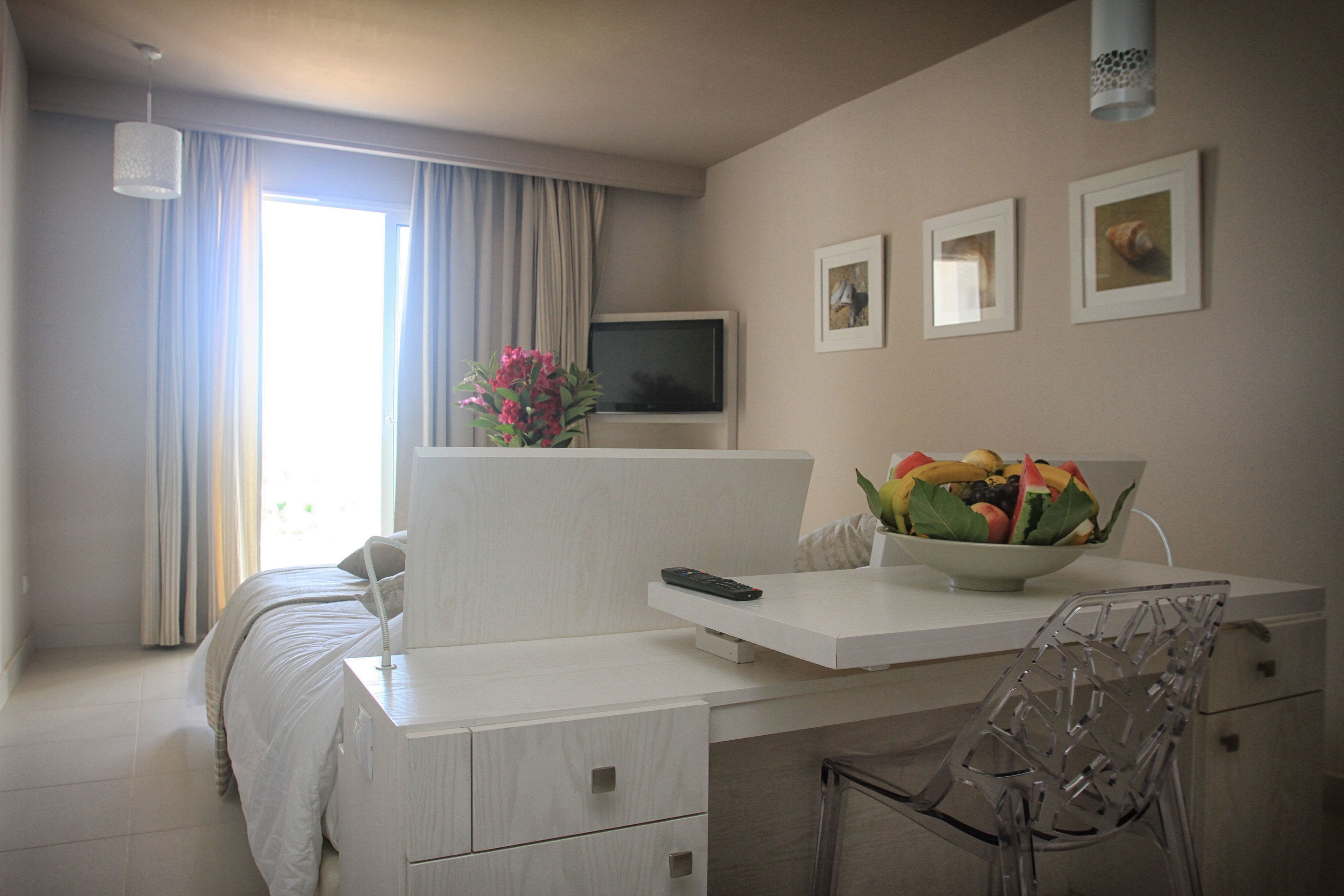 Une chambre d’hôtel moderne avec un lit, un bureau doté d’une télévision, une chaise et un panier de fruits posé sur le bureau.