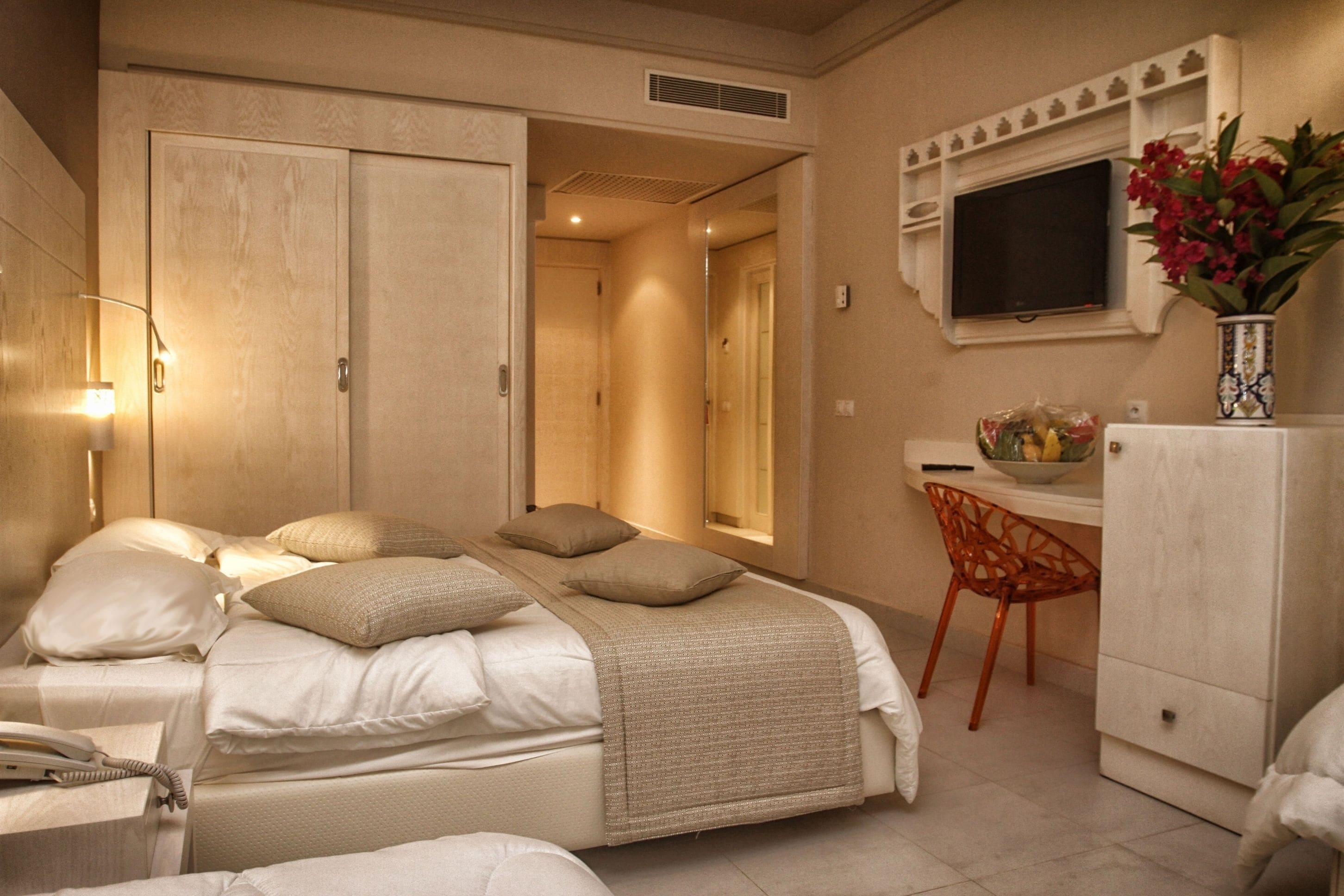 Una habitación de hotel con cama, mesita de noche, lámpara, escritorio, silla y televisor.