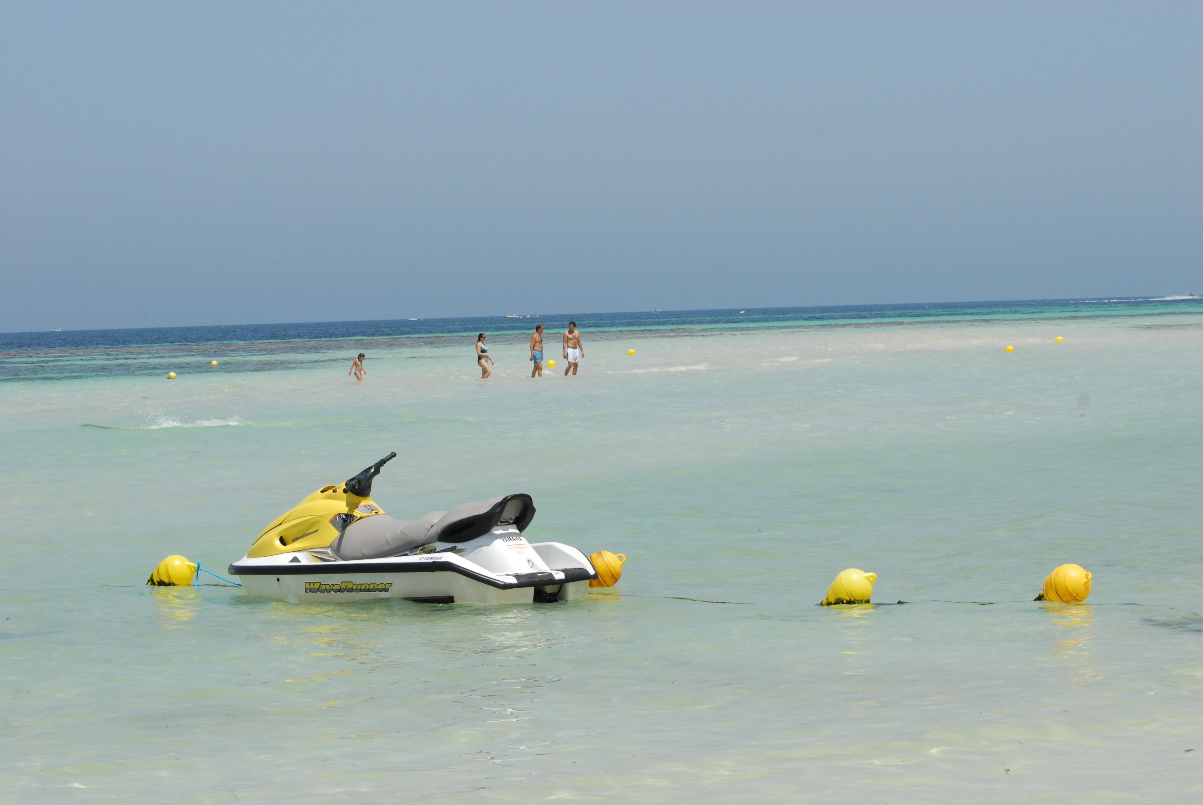 Un jet ski en una playa con aguas cristalinas y boyas amarillas.