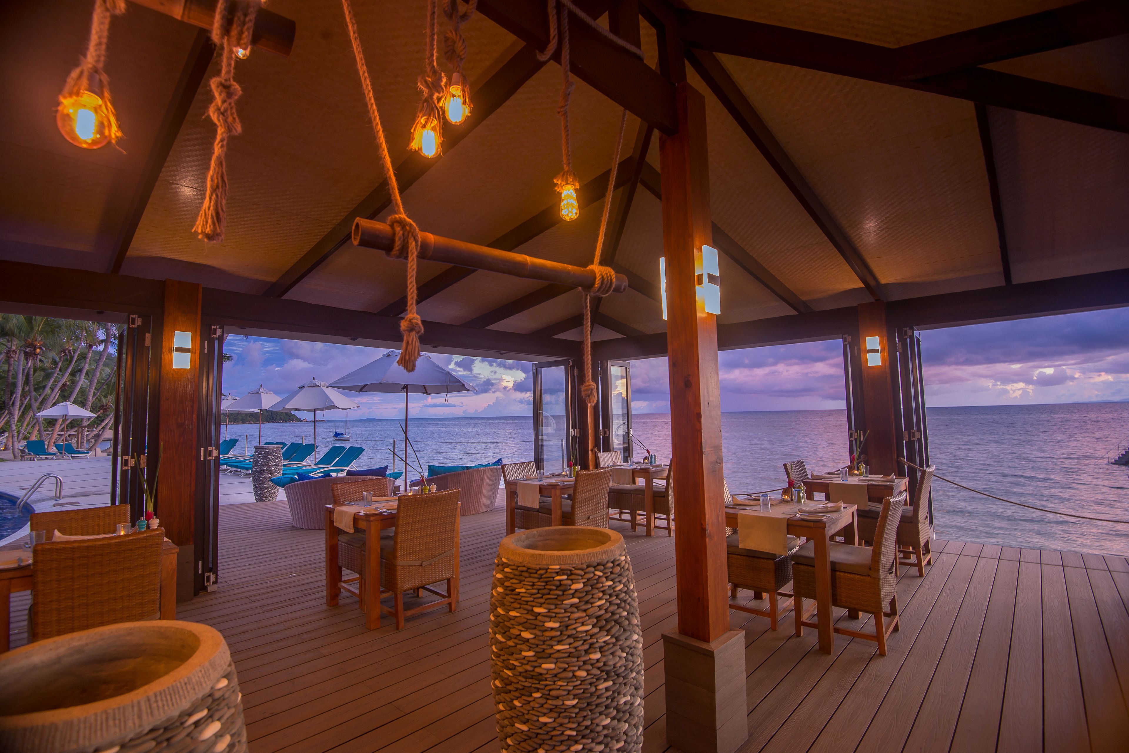 A wooden deck with tables and chairs, overlooking the ocean.