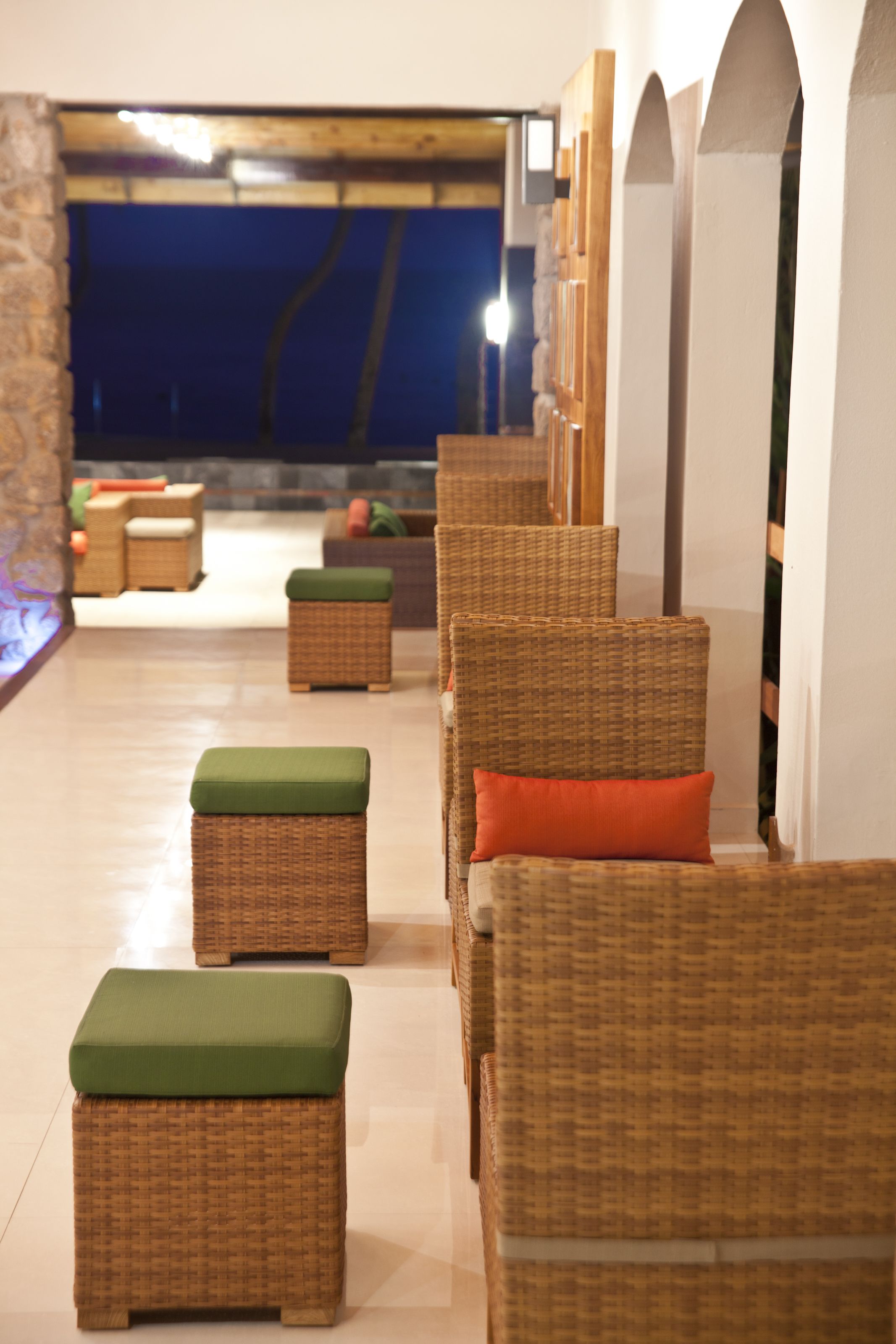 Wicker furniture with green and orange cushions in a well-lit indoor space with a view of the outside.