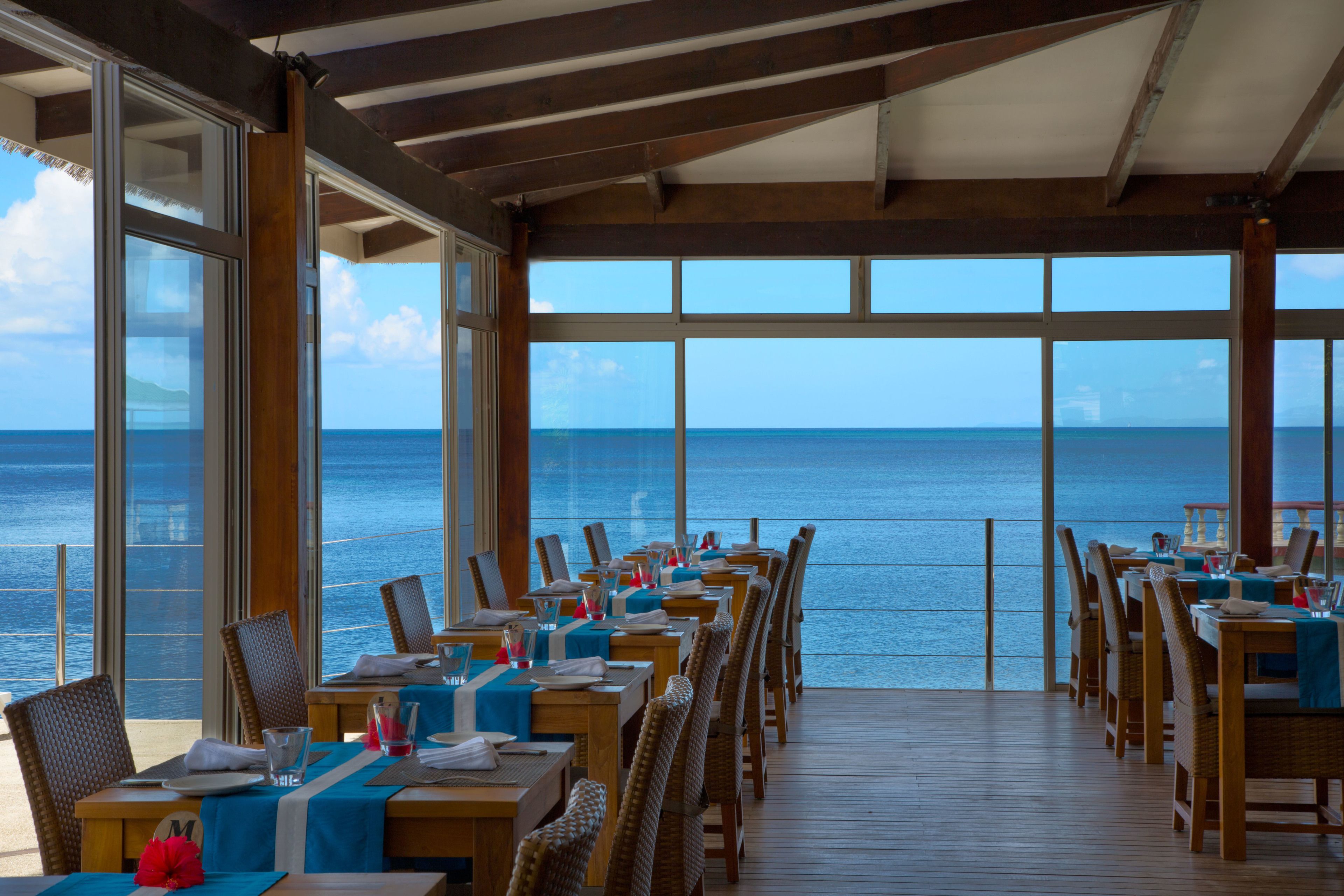 A restaurant with tables and chairs facing the ocean.