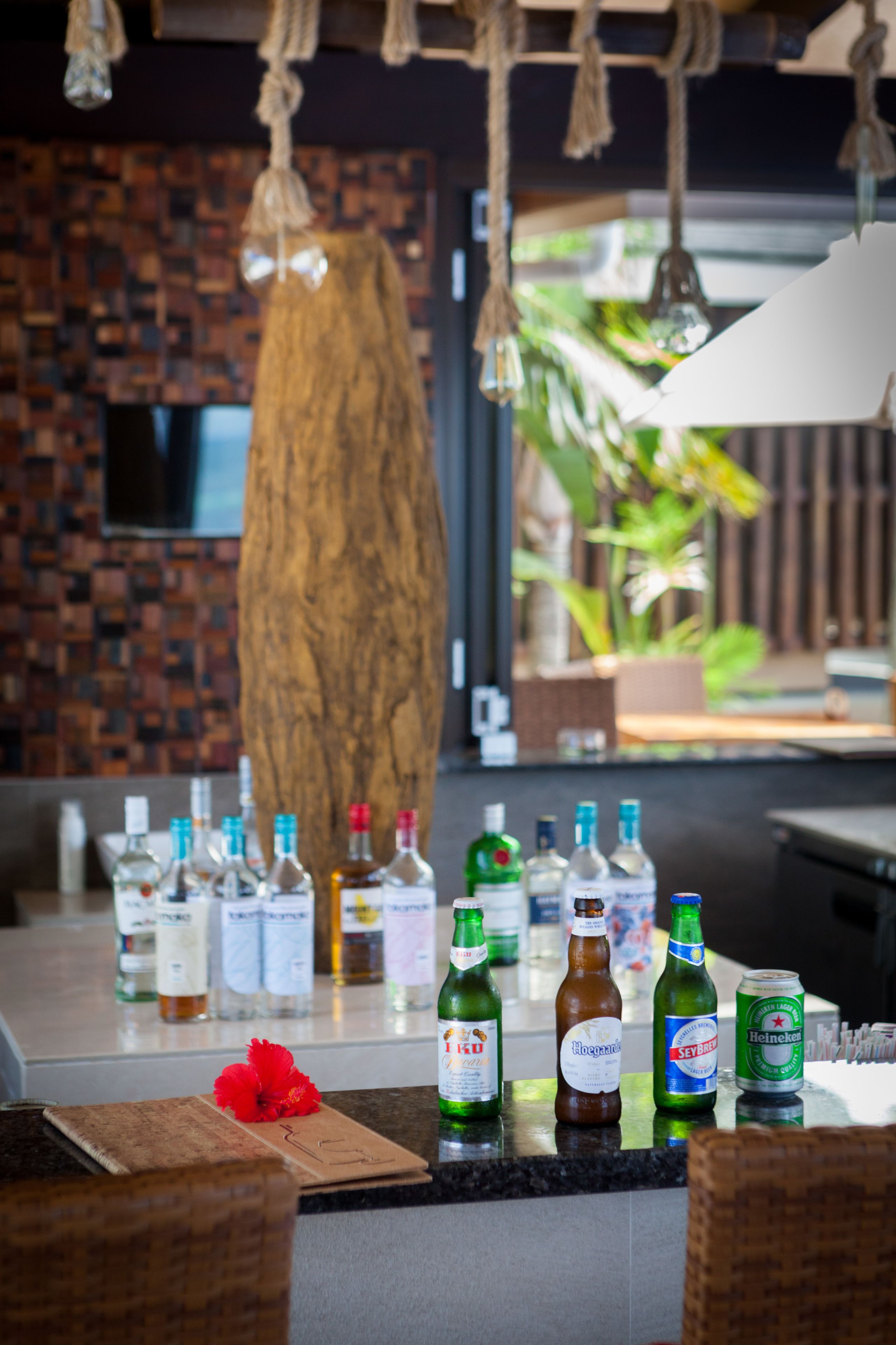 A bar area with bottles of alcohol, a wooden cutting board, and a red flower.