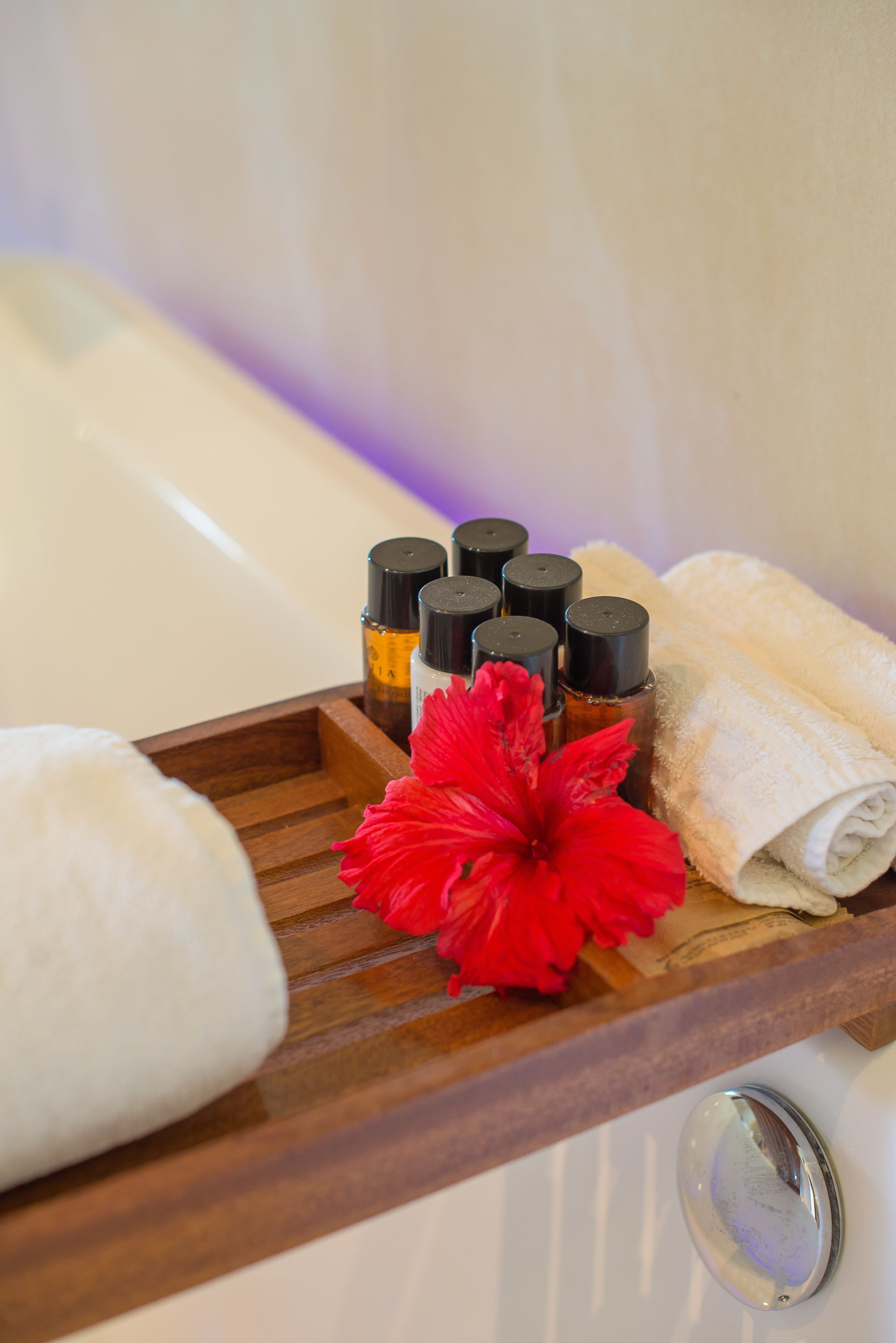 A wooden tray with toiletries and a red flower on a bathroom counter.