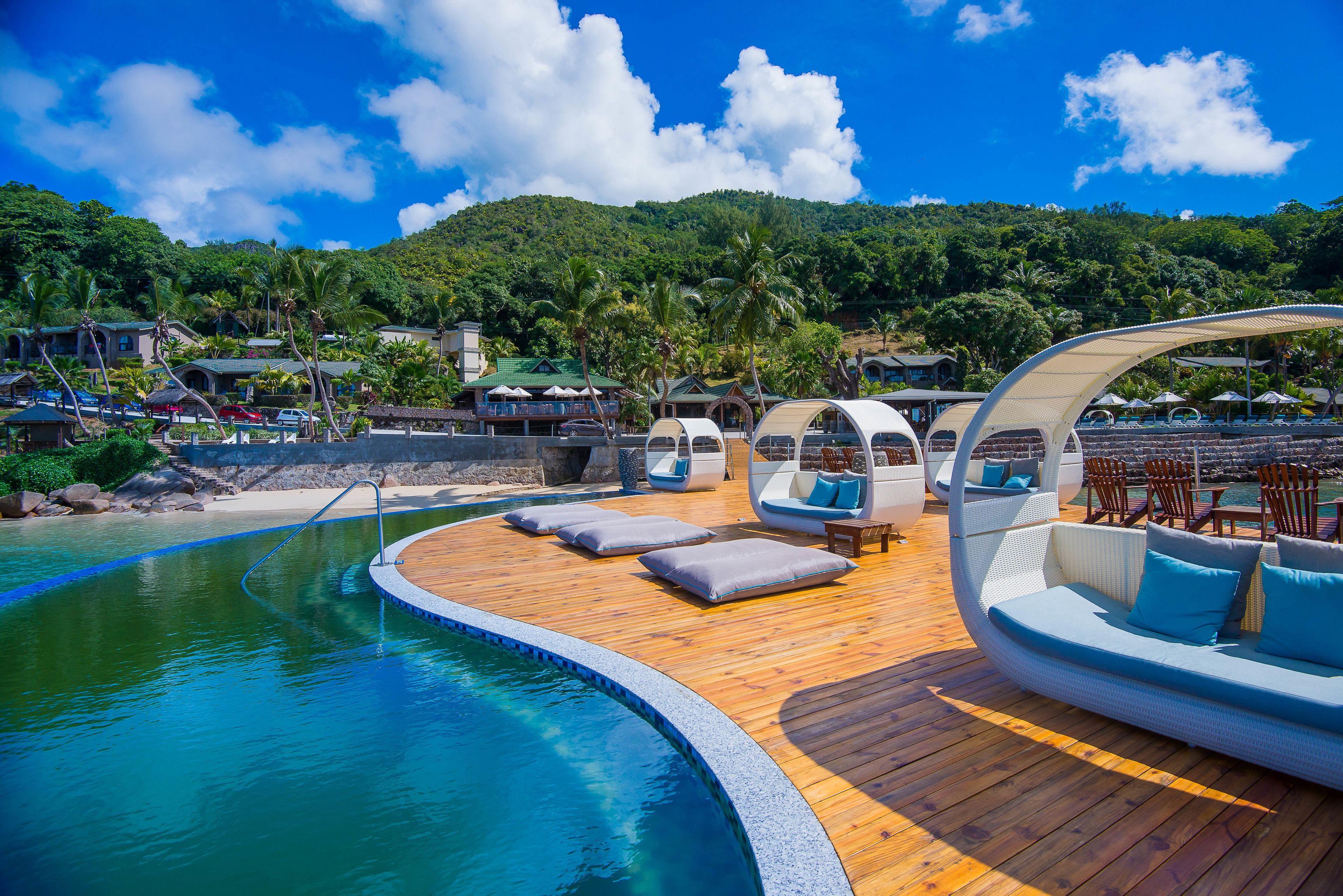 A poolside area with a wooden deck, lounge chairs, and a seating area with cushions.