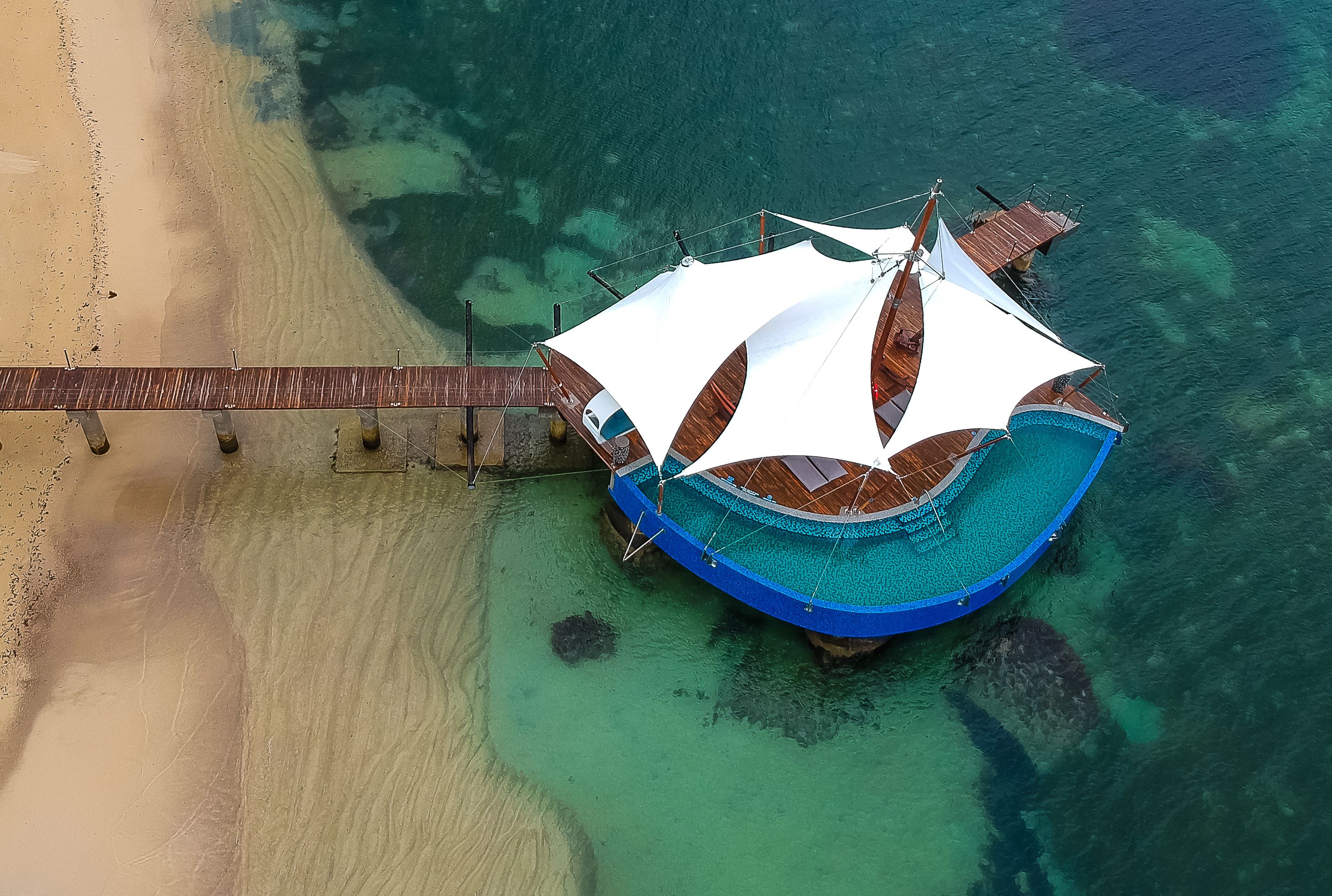 An overwater bungalows with a wooden deck and a white canopy, connected to the beach by a wooden walkway.