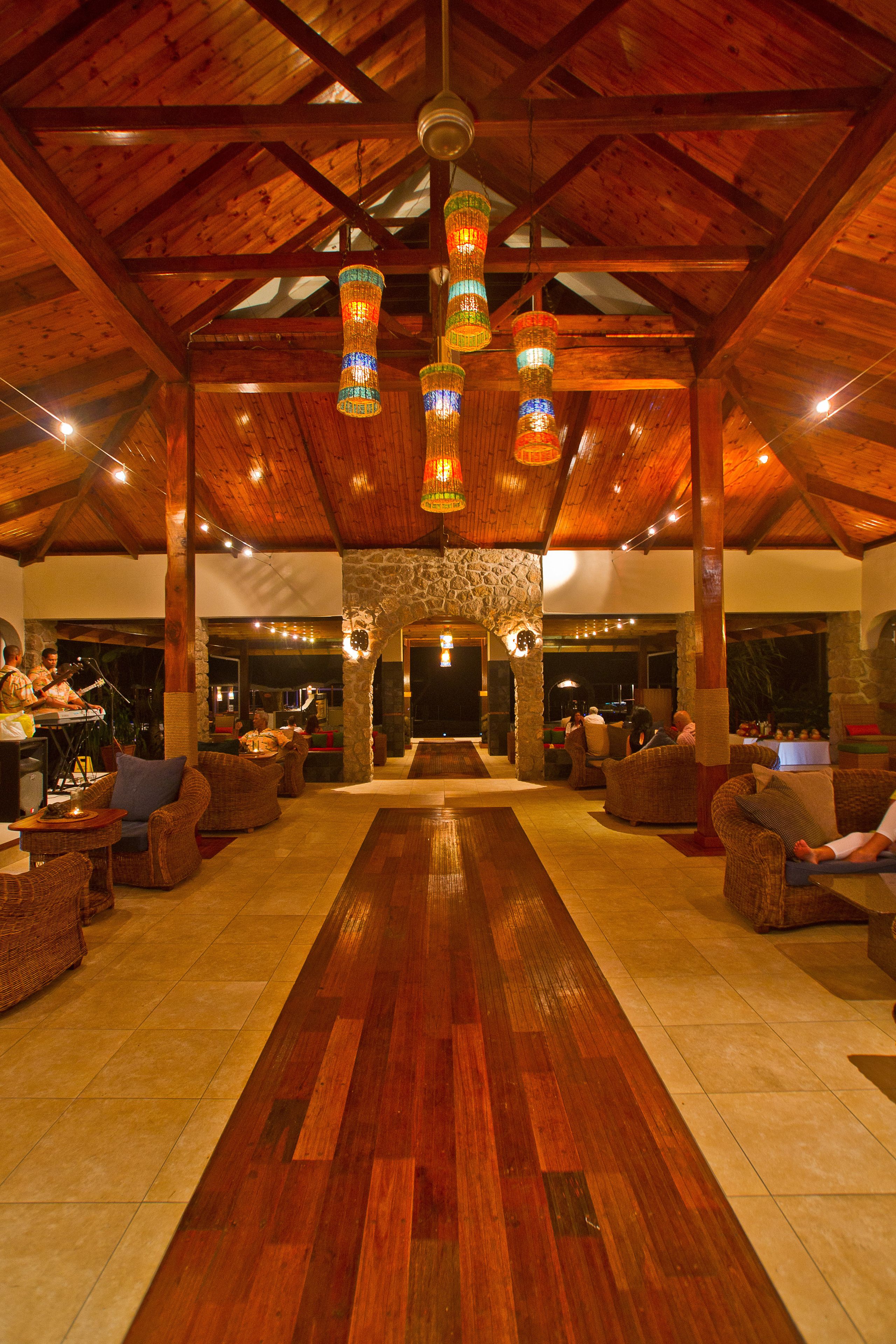 A spacious lobby with a wooden floor, wicker furniture, and hanging decorative lights.