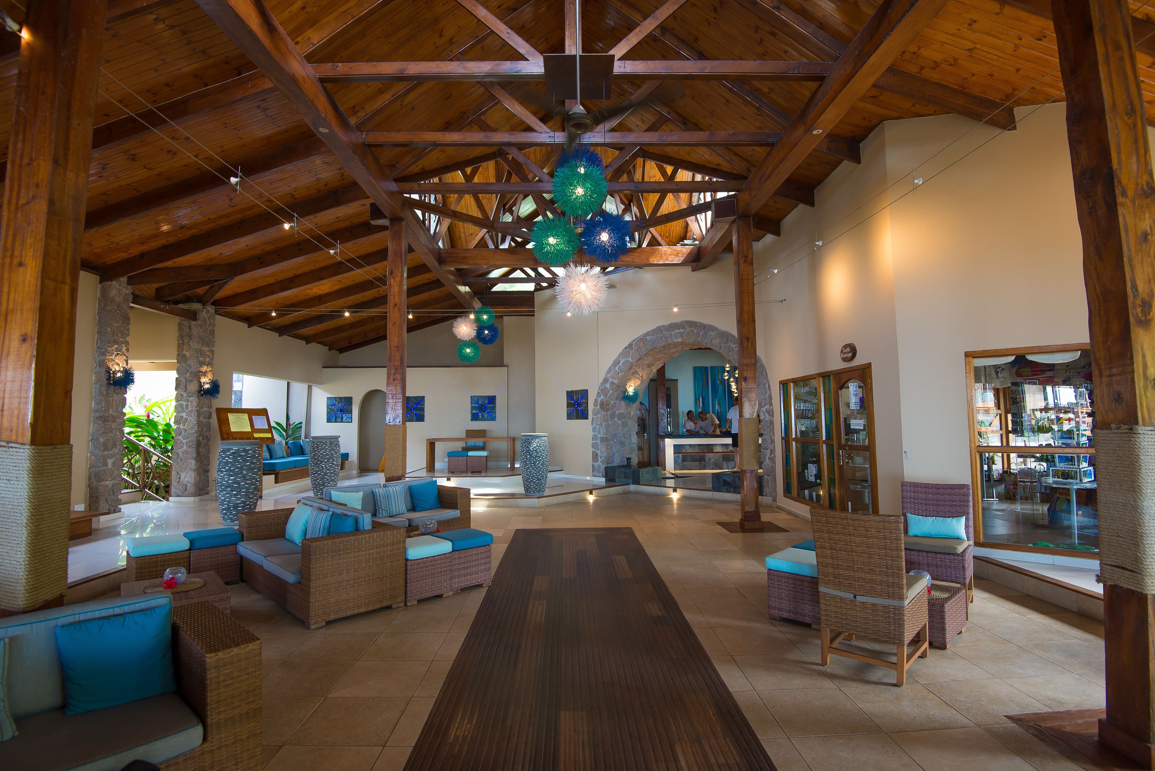 A spacious lobby with high ceilings, wicker furniture, and a central wooden table.