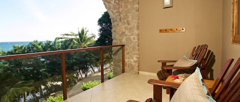 A balcony with a stone wall, wooden chairs, and a view of the ocean.