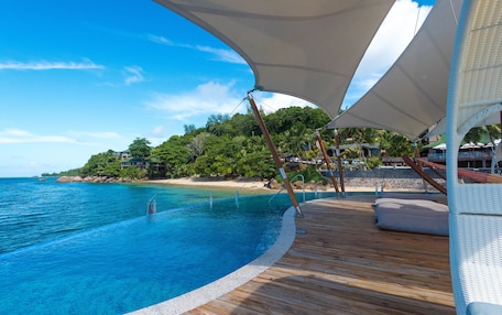 A wooden deck with a pool overlooking a beach and ocean.