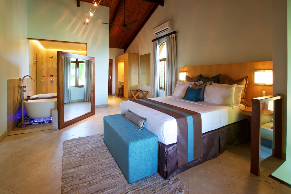 Een slaapkamer met een groot bed, houten plafond, een badkamer met douche en een spiegel.