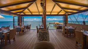 Een houten terras met tafels en stoelen, met uitzicht op de oceaan.