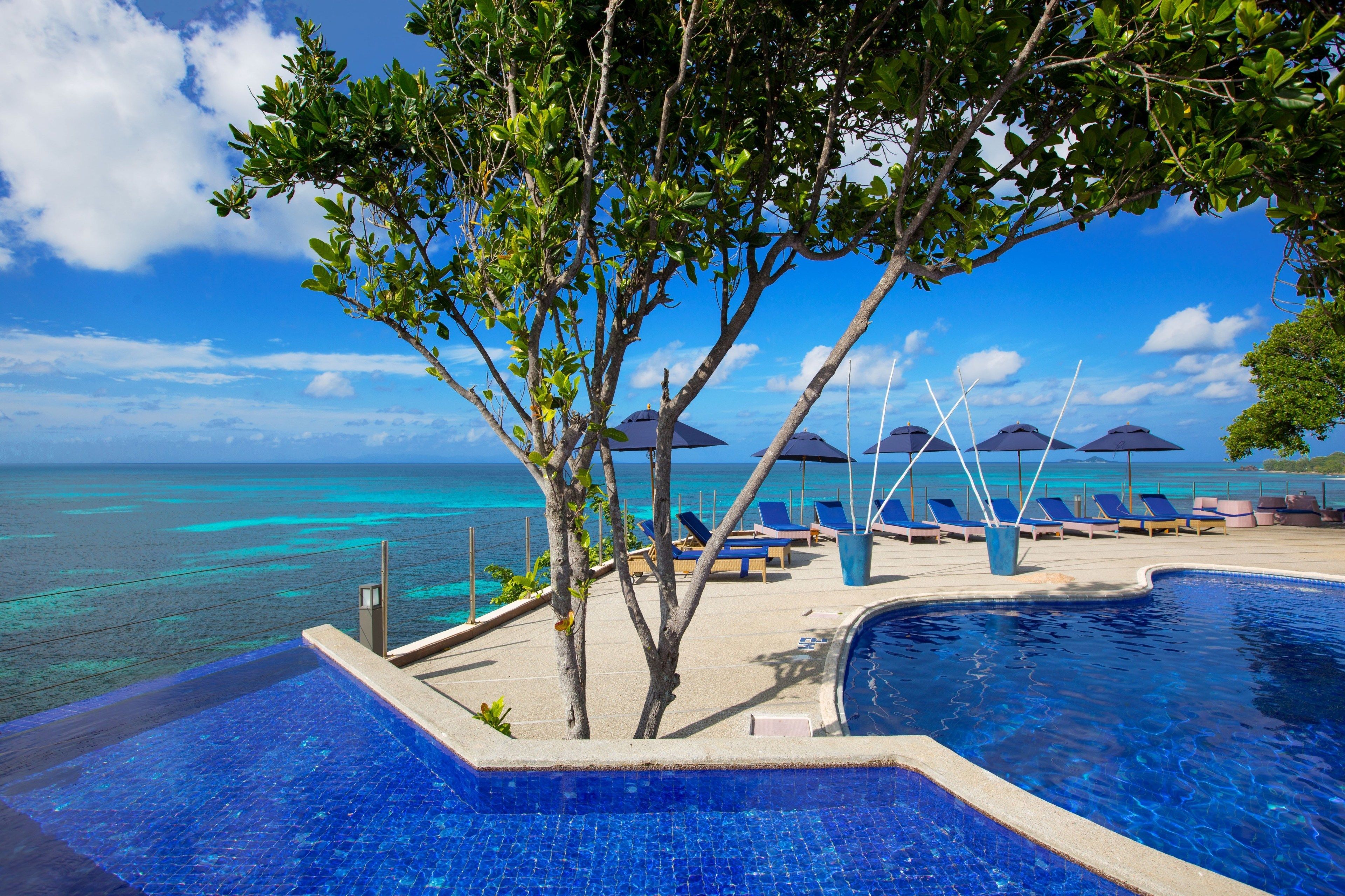 A pool area with lounge chairs and umbrellas, overlooking a turquoise sea.