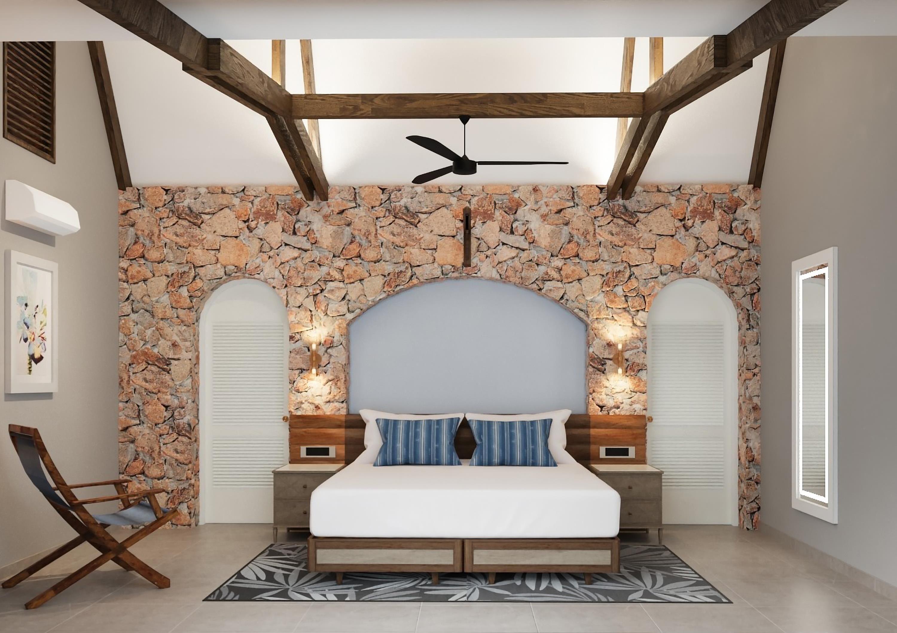 Un dormitorio con pared de piedra, una cama con cabecera de madera, dos mesitas de noche con lámparas, un ventilador de techo y una ventana.