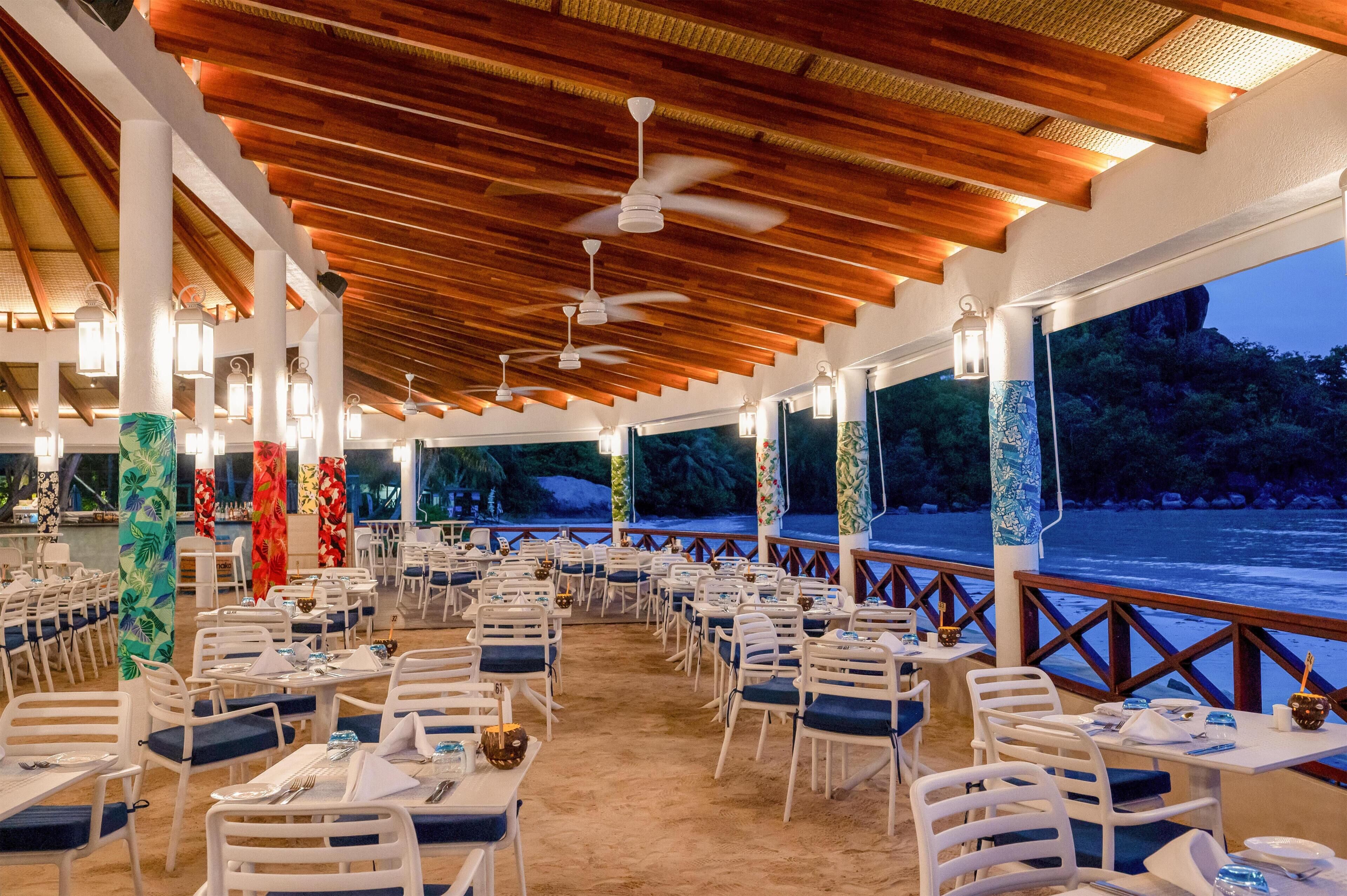 Un espacio al aire libre con mesas y sillas, ventiladores de techo y luces de estilo farol.