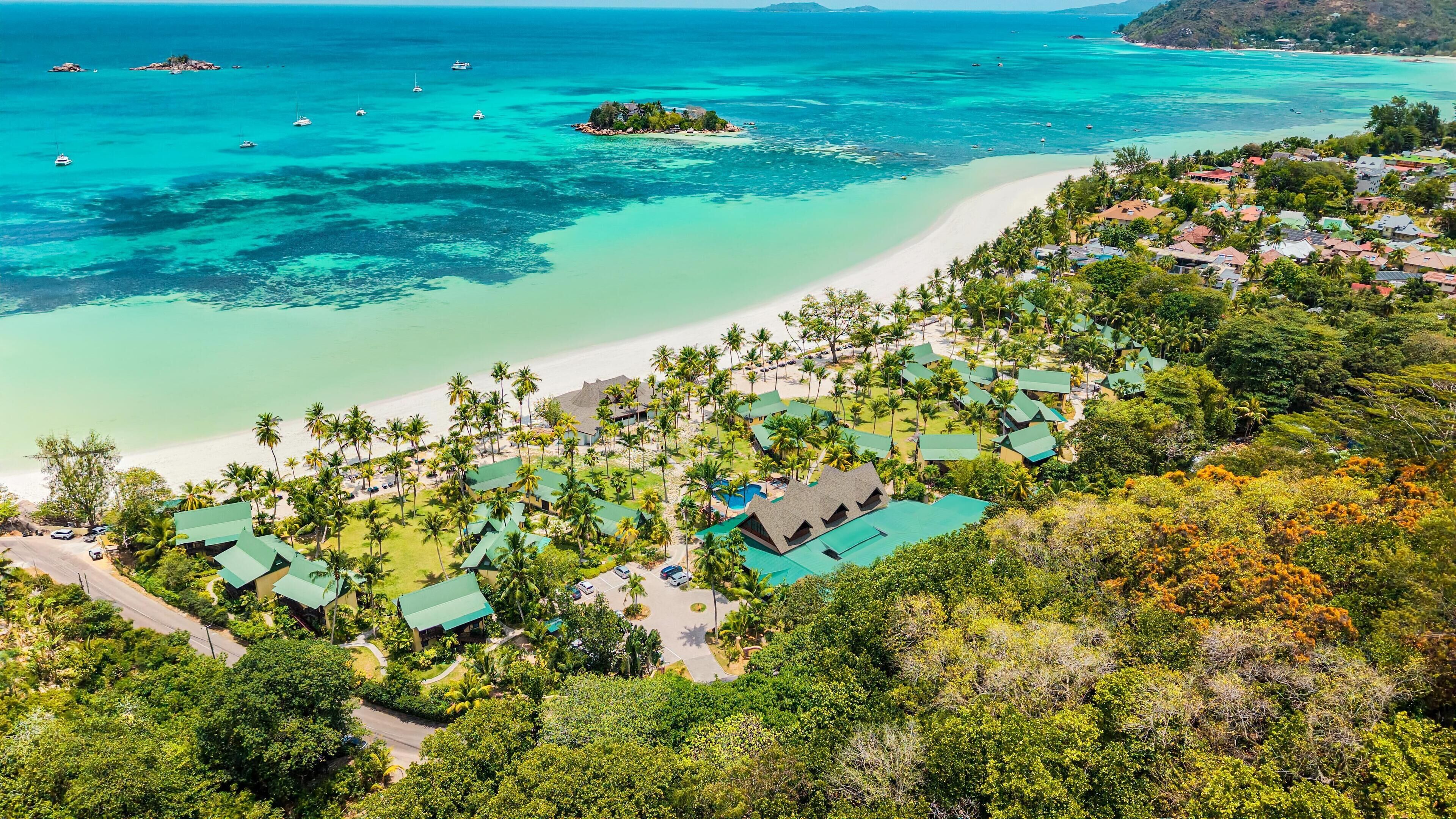 Un resort con varias construcciones tipo bungalow, una playa y aguas turquesas cristalinas con barcos.