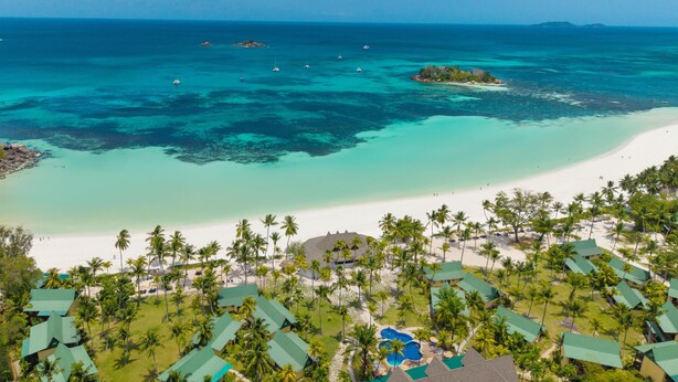 Un resort con varias construcciones tipo bungalow, una playa y aguas turquesas cristalinas.