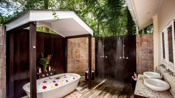 A modern outdoor bathroom with a freestanding bathtub, a shower enclosure, and two sinks. - Paradise Sun (Praslin Island)