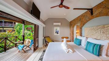 Un dormitorio con cama, ventilador de techo, televisor, balcón con una silla y vistas a zonas verdes.