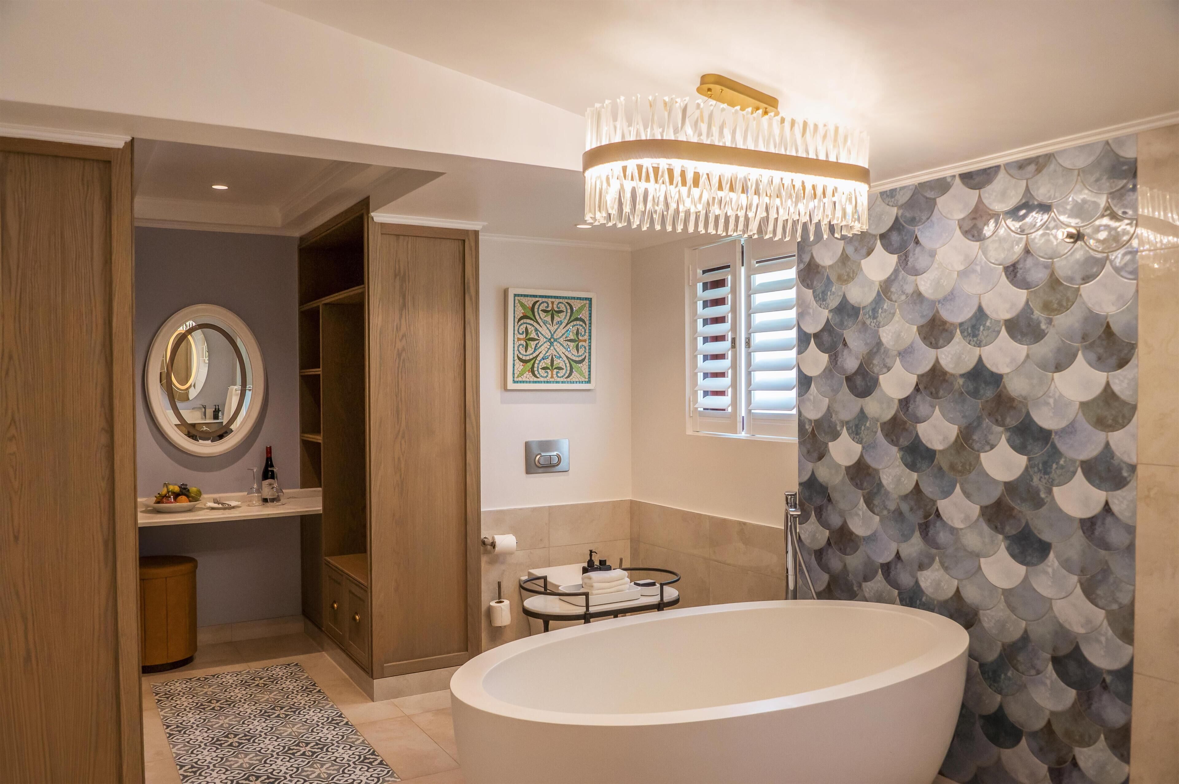 A modern bathroom with a freestanding bathtub, a round mirror, a towel rack, and a decorative wall panel.