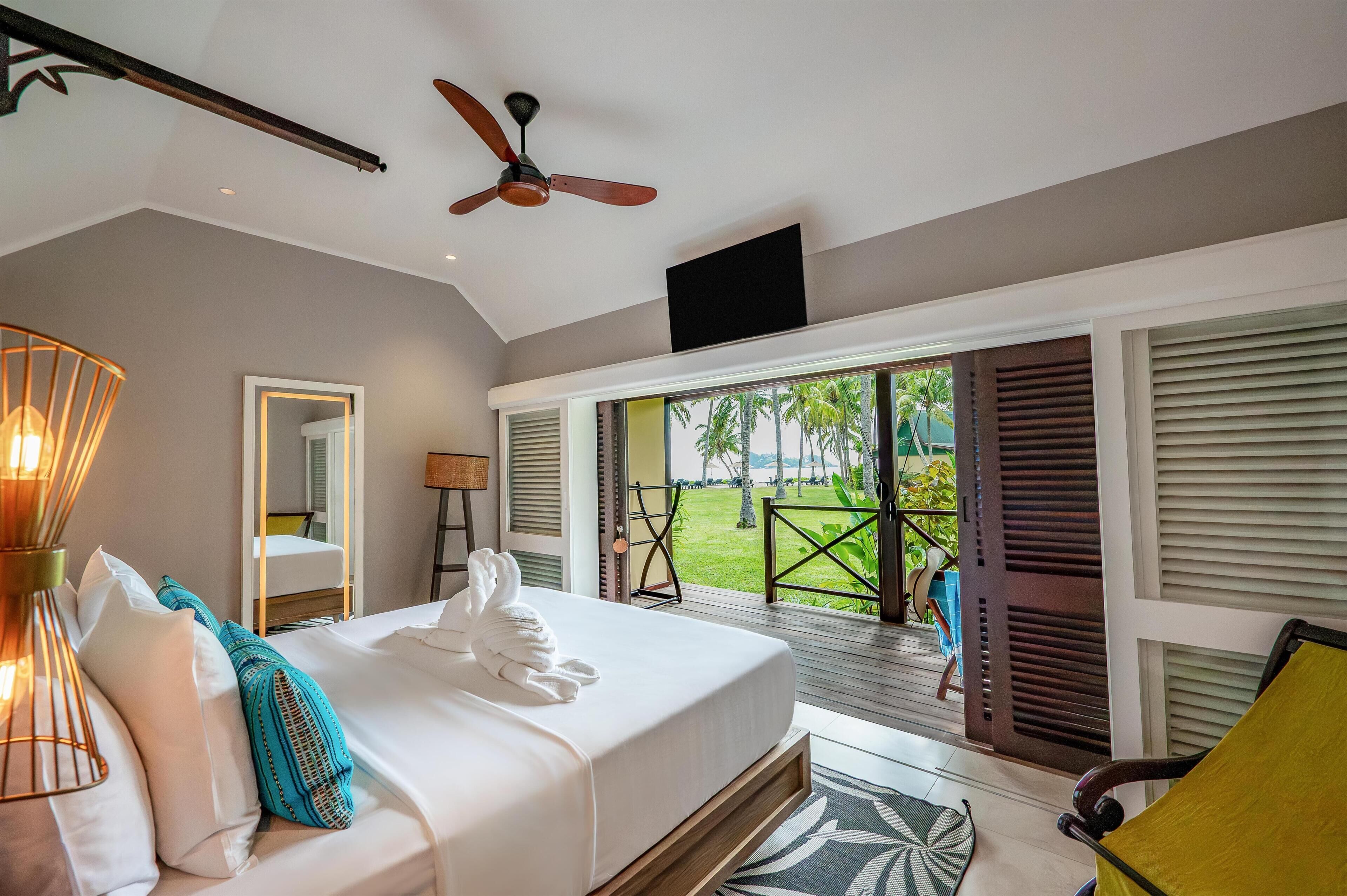 A bedroom with a bed, a ceiling fan, a window with a view of the outdoors, and a door leading to a balcony.