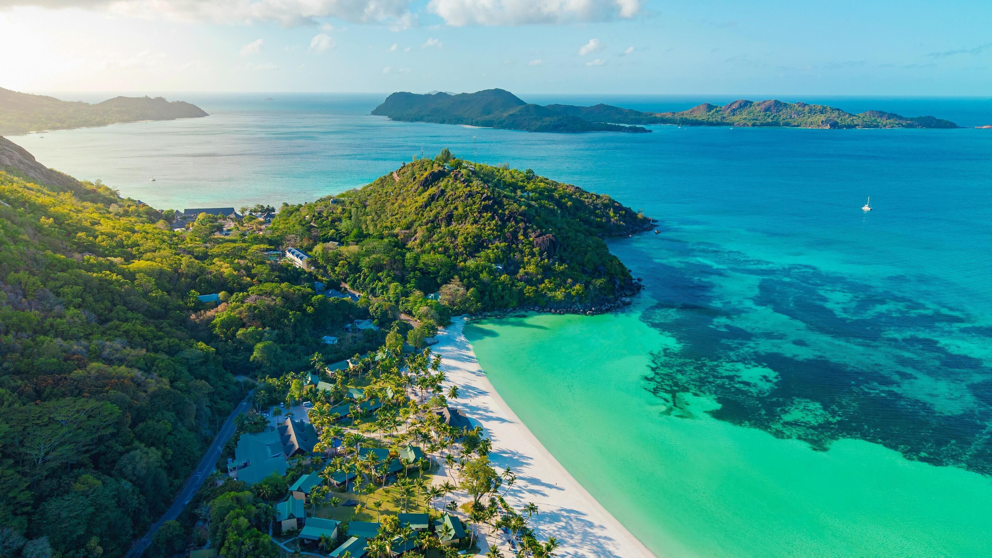 Vista aérea de una isla tropical con playa, aguas turquesas cristalinas y exuberante vegetación.