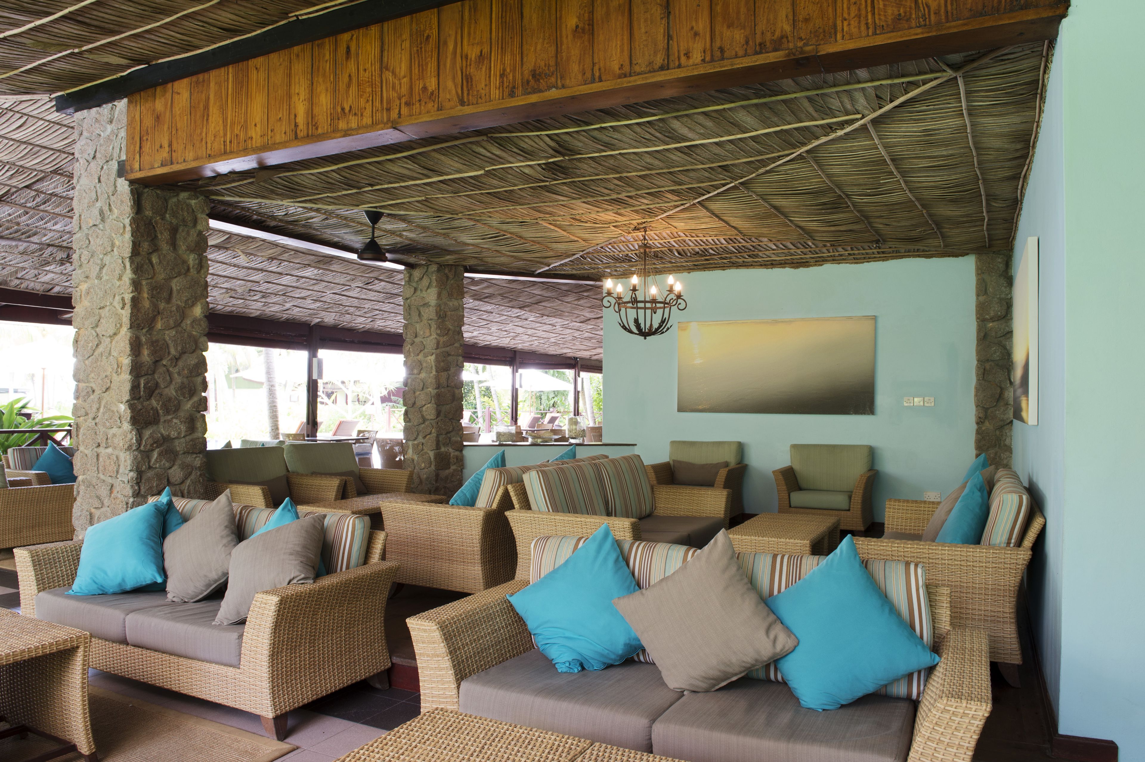 A lounge area with wicker sofas and chairs, stone pillars, a wooden ceiling, and a chandelier.
