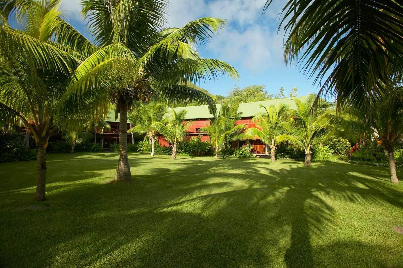 Un resort tropical con palmeras, un césped cuidado y un edificio de techo rojo.