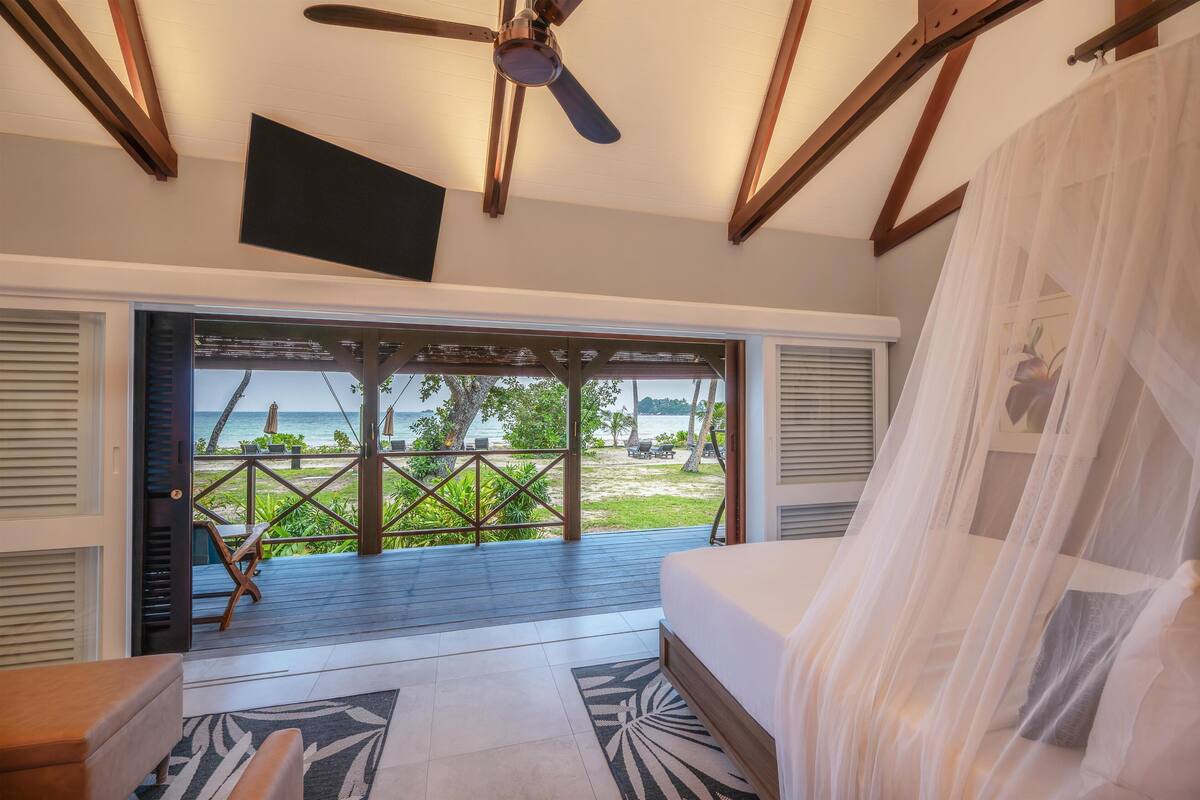 Ein Schlafzimmer mit einem Bett, einem Deckenventilator, einem Fernseher und Blick auf den Strand.