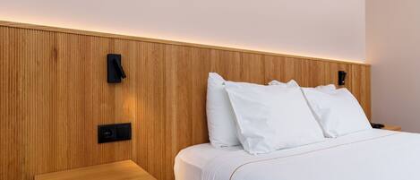 A hotel room with a wooden headboard, a bedside table, and a bed with white bedding.