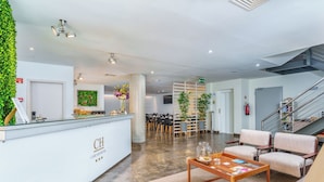 Zona de recepción de un hotel con mostrador, asientos, una escalera y una planta en la pared.