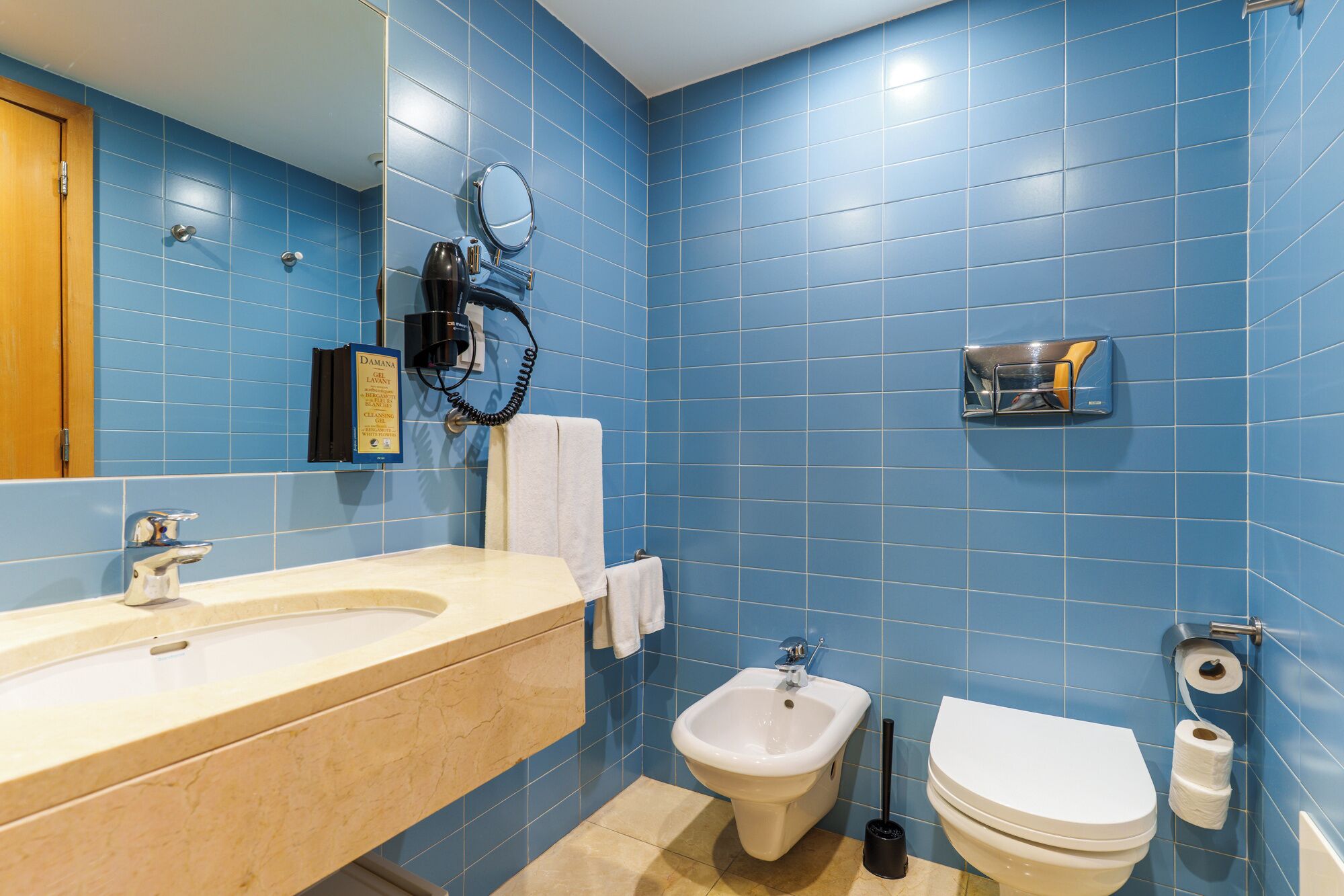 Une salle de bain avec des carreaux bleus, un lavabo, un bidet, des toilettes, un porte-serviettes et un miroir.