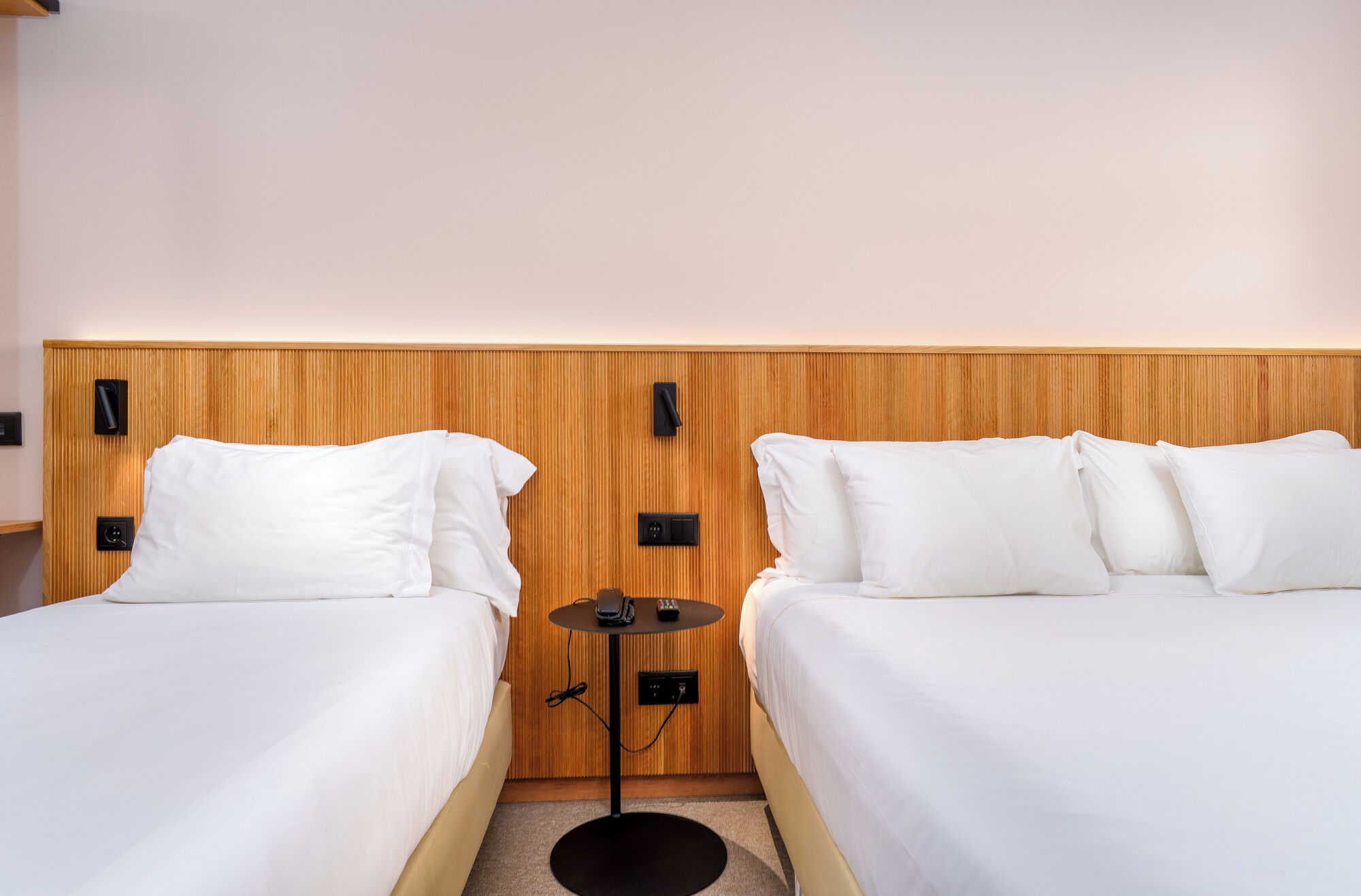 Habitación de hotel con dos camas, una mesita pequeña y un panel de control en la pared.