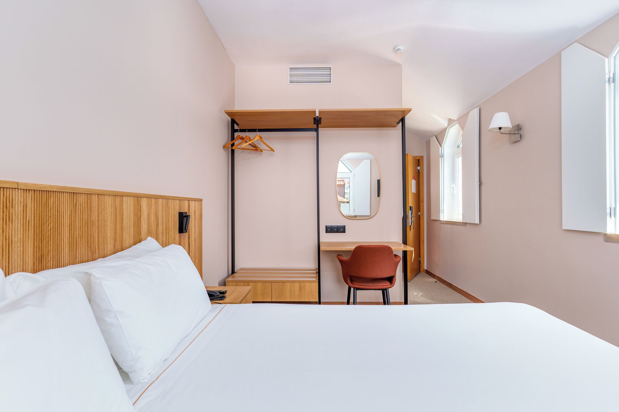 A hotel room with a bed, a desk, a chair, a mirror, and a wardrobe.
