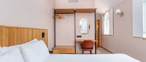 A hotel room with a bed, a desk, a chair, a mirror, and a wardrobe.