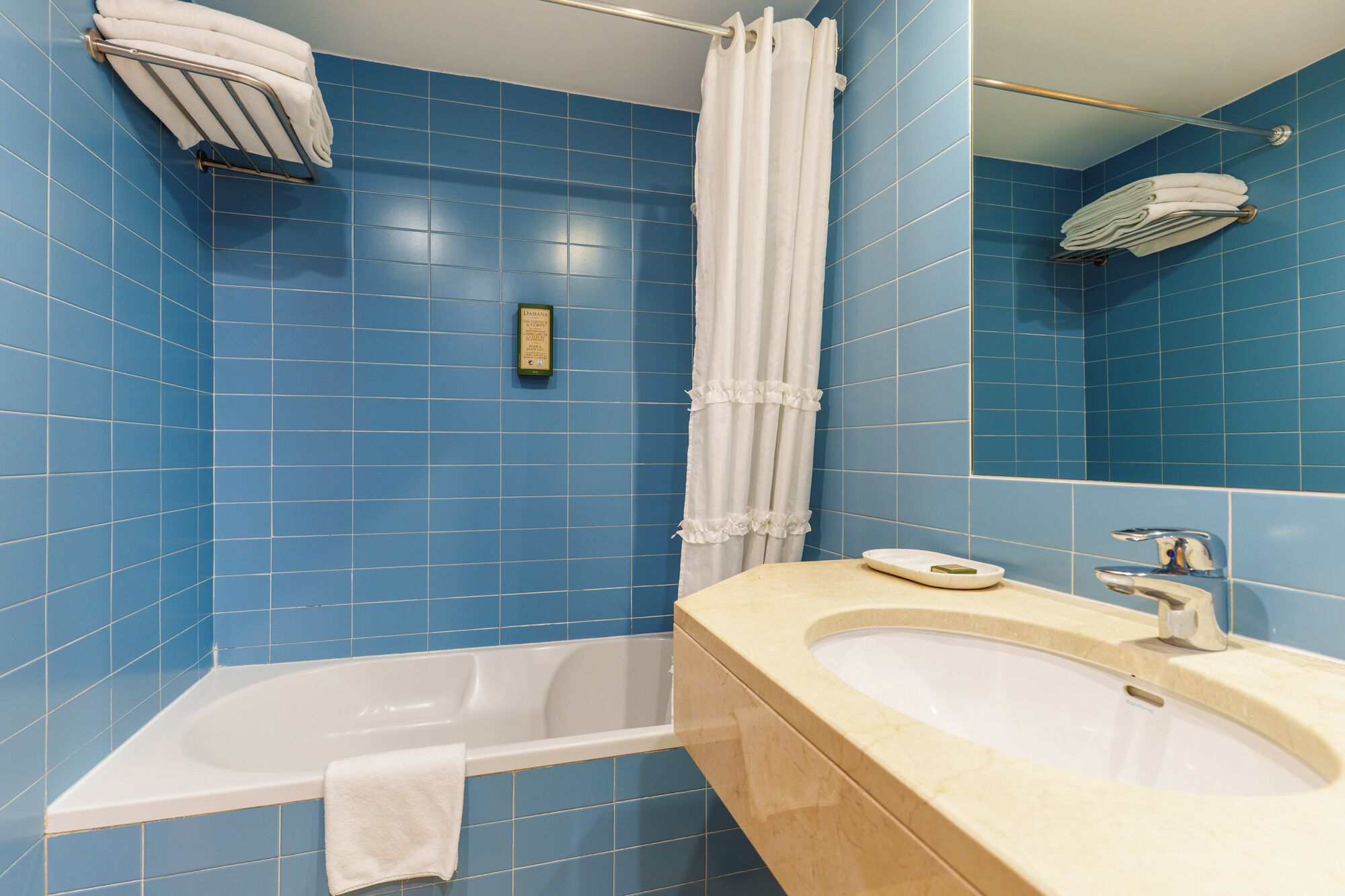 A bathroom with blue tiles, a bathtub, a sink, a towel rack, and a shower curtain.