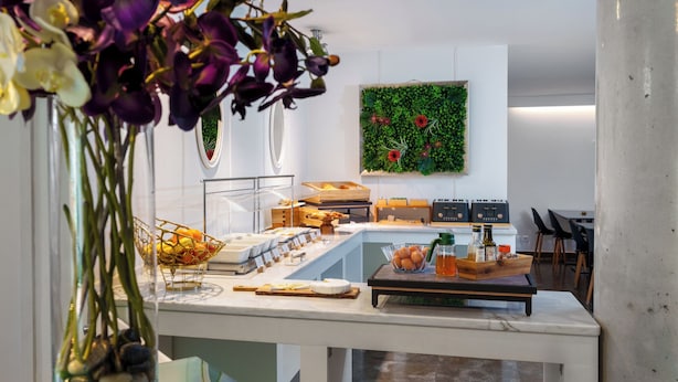 Un bufé de desayuno con diversos alimentos, una pared verde con plantas y una cocina moderna.