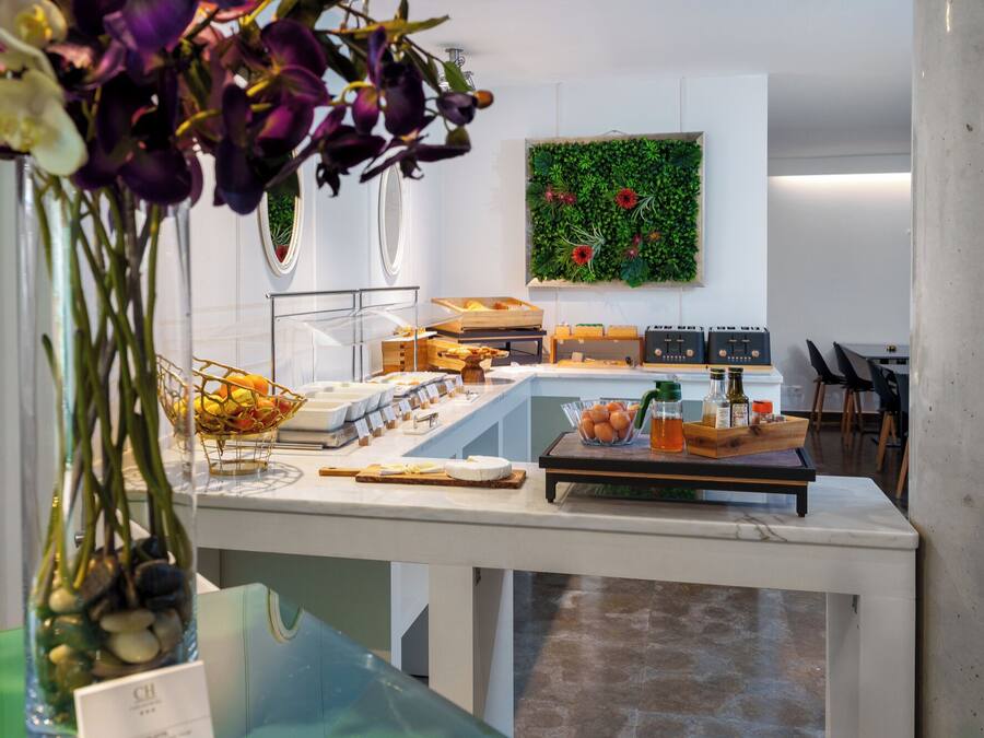 Um buffet de café da manhã com diversos alimentos, uma parede verde com plantas e uma área de cozinha moderna.