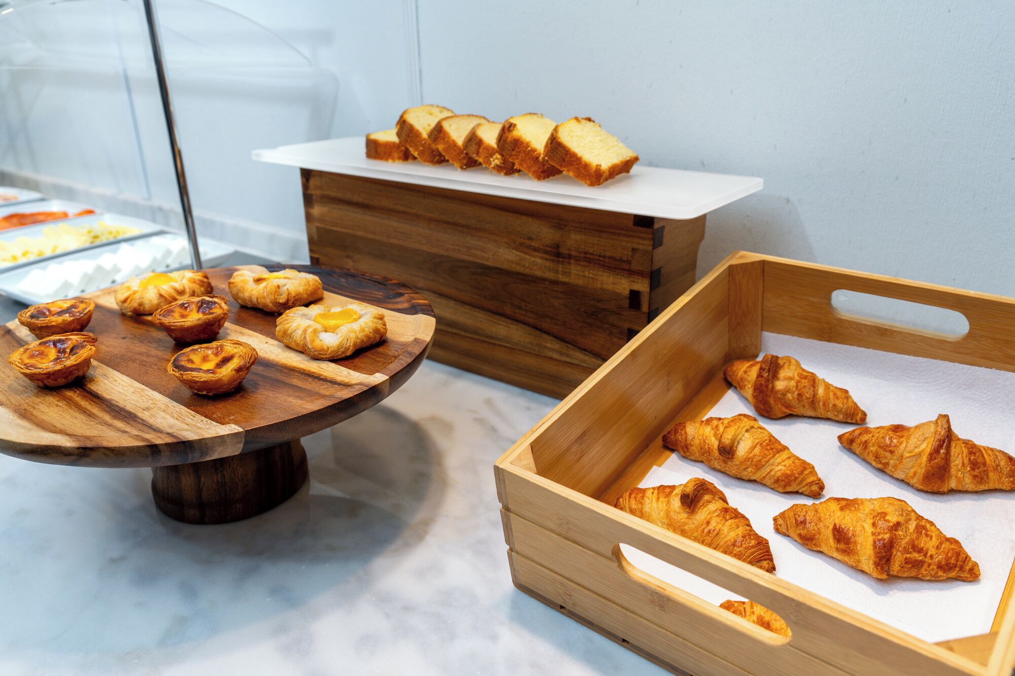 Un bufé con diversas pastas, incluyendo tartas y croissants, dispuestas sobre tablas de madera y en una caja de madera.