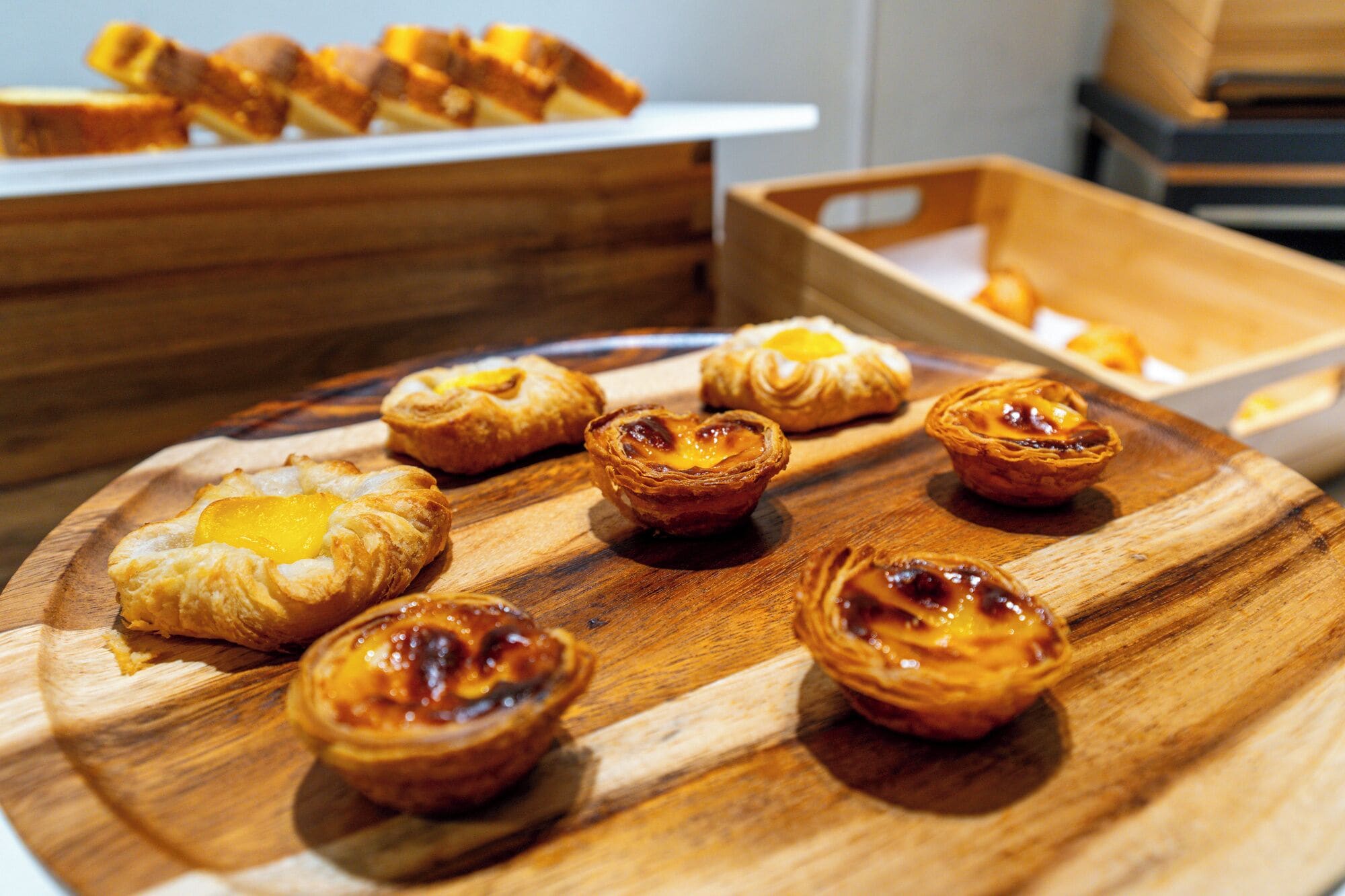 Ein Holzboden mit verschiedenen kleinen Gebäcken, vermutlich portugiesischen Pastéis de Nata, auf einem Tisch.