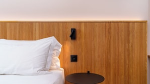 Una cama con sábanas blancas, una mesa redonda y una pared de madera con dos interruptores negros.