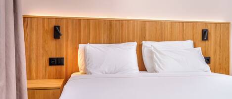A hotel room with a wooden headboard, two white pillows, a wooden nightstand, and a wall-mounted light fixture.