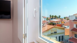 Una habitación con un ventanal grande, un televisor de pantalla plana en la pared y vistas a un pueblo costero con edificios de tejados de terracota.